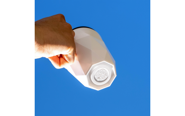 Hand hält einen weißen, facettierten Becher vor blauem Himmel