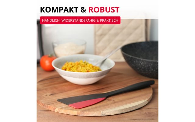 Spatule noire avec tête rouge sur une planche à découper ronde en bois ; en arrière-plan un bol de riz jaune avec une cuillère, une poêle noire, une tomate, un bol de céréales et un manique beige ; en haut à gauche des bandeaux de texte 'KOMPAKT & ROBUST' et 'HANDLICH, WIDERSTANDSFÄHIG & PRAKTISCH'