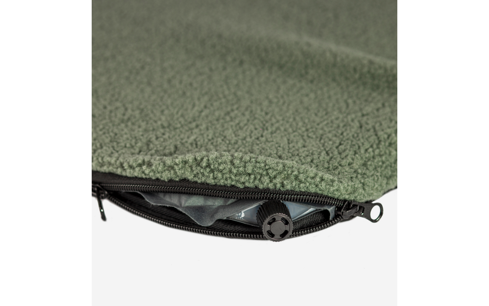 Grüner Fleece-Stoff mit teilweise offenem Reißverschluss, sichtbar rundes schwarzes Kunststoffteil mit vier Aussparungen und gemustertes Innenfutter