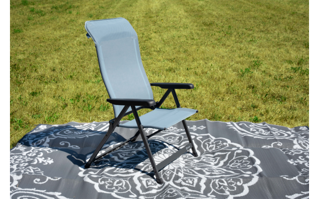 Sedia pieghevole azzurro chiaro con struttura nera e braccioli su un tappeto grigio con motivo floreale bianco, davanti a erba verde