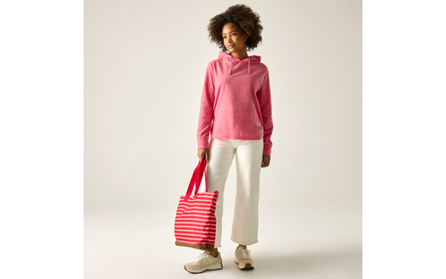Person mit lockigen Haaren trägt rosa Kapuzenpullover und weiße weite Hosen, hält eine rot-weiß gestreifte Tasche in der linken Hand, steht vor hellem Hintergrund, trägt beigen Sneaker