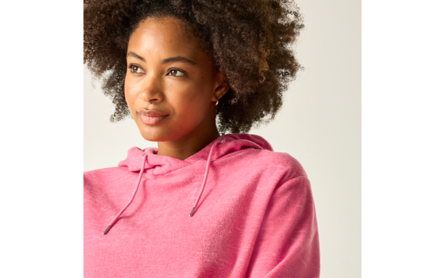 Person mit lockigem Haar trägt rosa Kapuzenpullover, blickt nach links vor hellem Hintergrund
