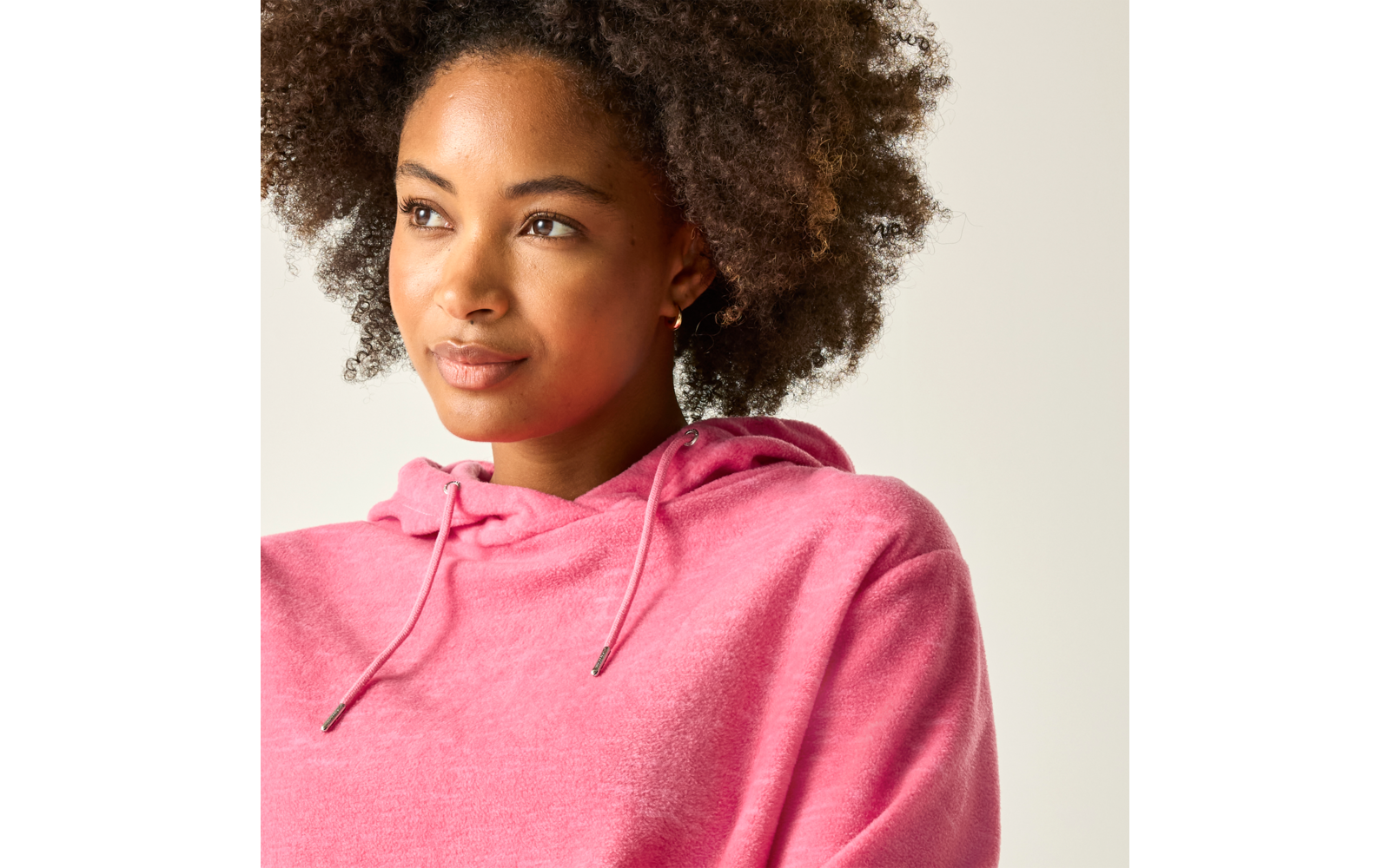 Person mit lockigem Haar trägt rosa Kapuzenpullover, blickt nach links vor hellem Hintergrund
