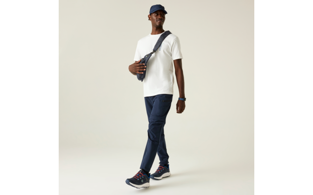 Persona caminando, viste camiseta blanca, pantalones azul oscuro, gorra oscura, bolso cruzado, zapatillas azul oscuro con suelas blancas, reloj de pulsera