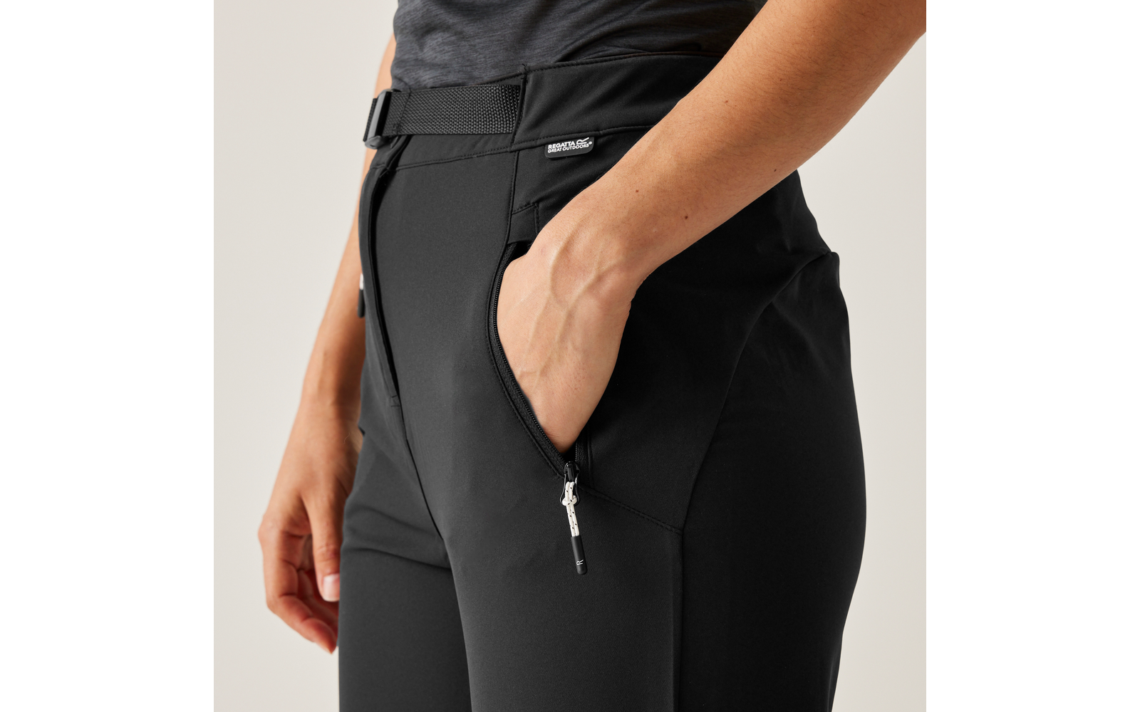 Eine Hand steckt in der Seitentasche einer schwarzen Hose mit Reißverschluss