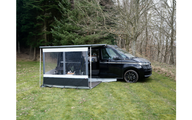 Schwarzer Campervan mit geöffneter Seitentür und angebautem transparenten Vorzelt auf einer Wiese vor Bäumen ohne Blätter