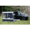 Black camper van with open side door and attached transparent awning on a grassy area in front of leafless trees