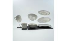 Tasses blanches, assiettes et un bol sur un tapis noir, quelques assiettes flottent en arrière-plan
