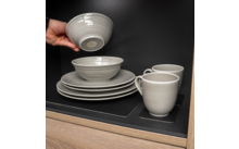 Main tenant un bol au-dessus d'assiettes et de tasses empilées dans une armoire
