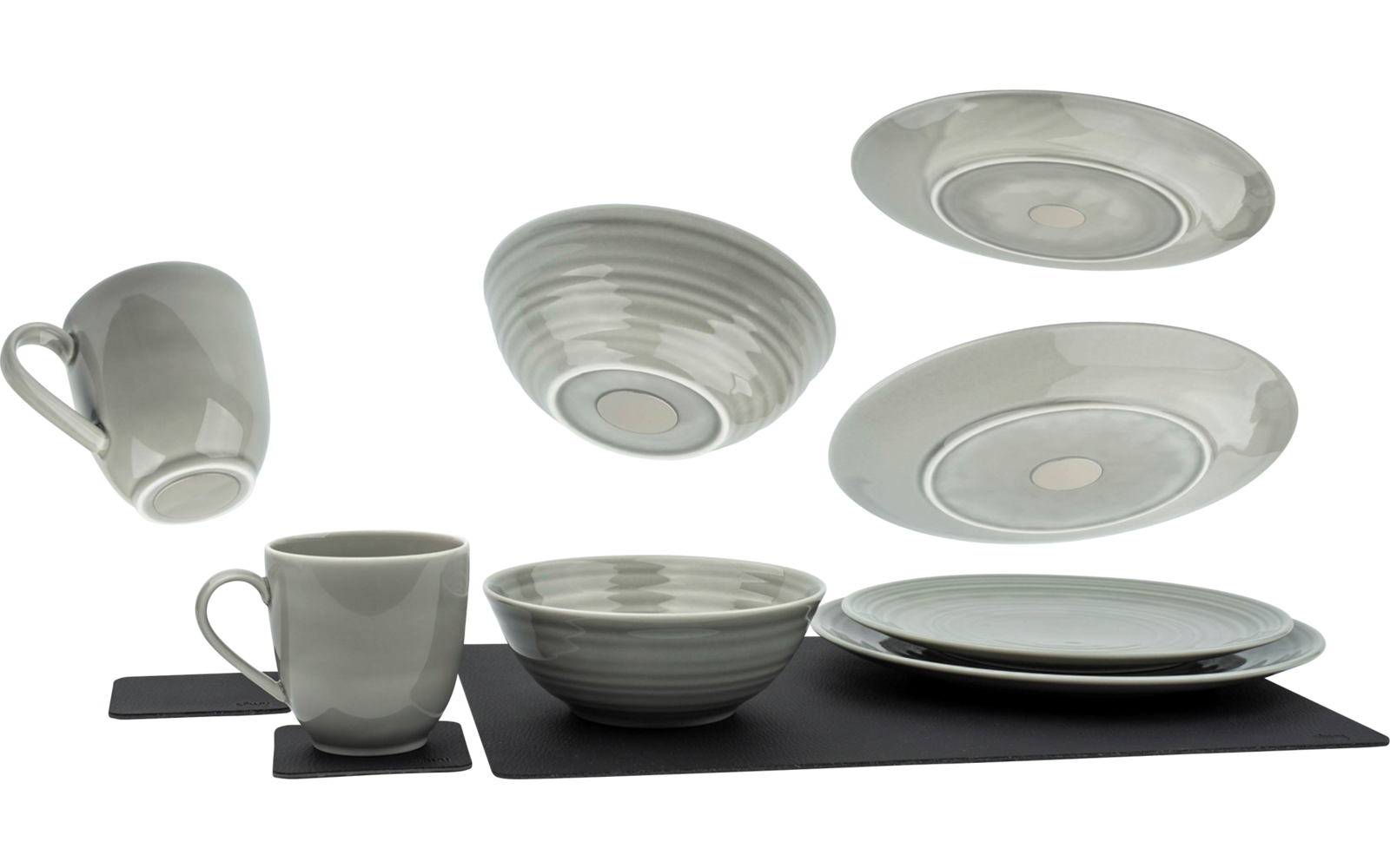 Witte kopjes, borden en een kom op een zwarte onderlegger, enkele borden zweven op de achtergrond