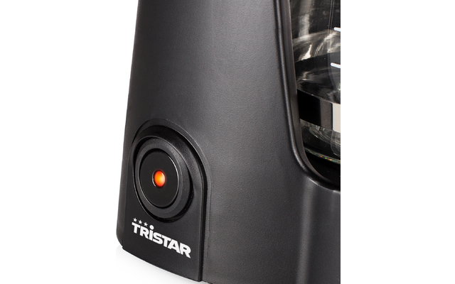 Gros plan de la base noire d'un boîtier de cafetière avec un bouton rond illuminé orange, le logo blanc "TRISTAR" et une partie d'une verseuse en verre
