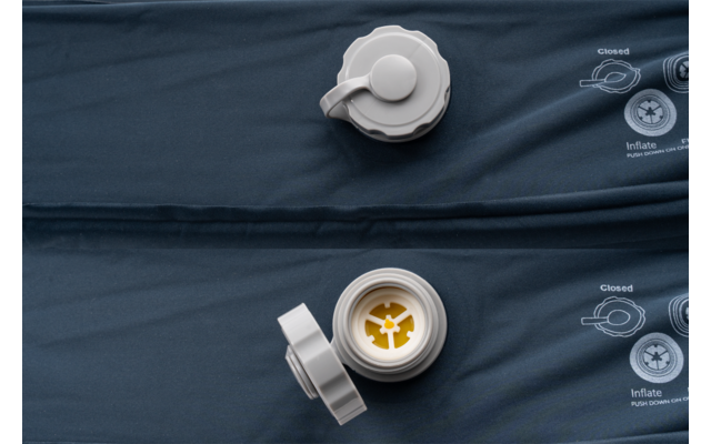 Dunkelblauer aufblasbarer Mattenstoff mit zwei weißen Kunststoffventilen, eines geöffnet mit gelbem Innenstück, eines verschlossen; gedruckte Piktogramme rechts