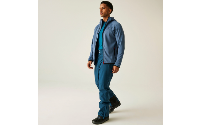 Mann im blauen Hemd, dunkler Jacke und Jeans steht auf hellgrauem Hintergrund