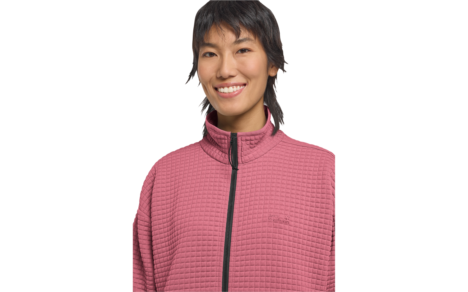 Nahaufnahme einer lächelnden Person mit kurzem dunklem Haar, rosa gesteppte Jacke mit Reißverschluss, weißer Hintergrund