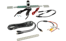 Mehrere elektronische Kabel und Adapter; oben ein kleines weißes Gehäuse mit zwei runden Linsen auf einer durchsichtigen Leiste; rote und schwarze Stromkabel; Bündel schwarzer Kabel; USB‑ und Cinch‑Stecker (gelb/rot/weiß); zwei Metallkrokodilklemmen;