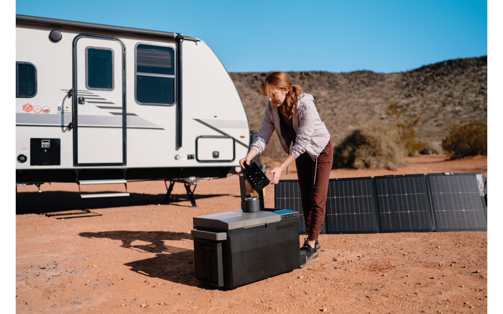 Frau richtet Solarpanel neben Wohnmobil in sonniger Umgebung ein