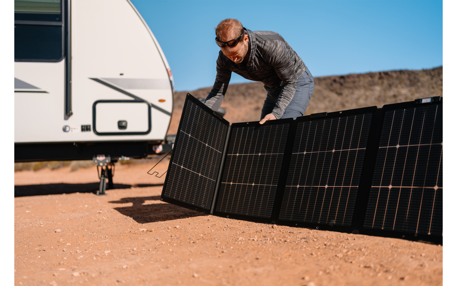 Mann montiert Solarpanels auf Boden vor Wohnmobil