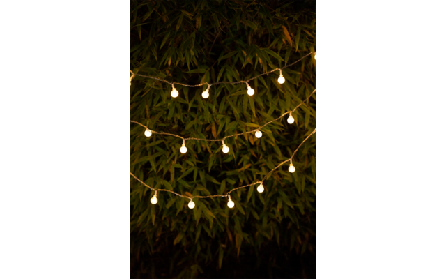 Frau sitzt am Café-Tisch und lächelt, im Hintergrund Blumen und Holztisch