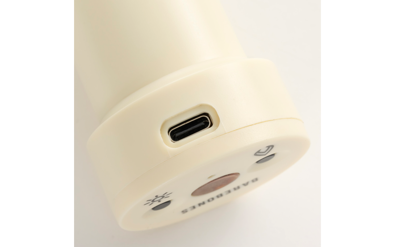 Close-up van de onderzijde van een crèmekleurig cilindrisch apparaat met een USB-C-poort in een ovaal uitsparing, een ronde basis met meerdere opgedrukte symbolen en een ronde knop