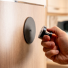 Hand houdt een zwarte magnetische meubelknop voor een licht houten oppervlak