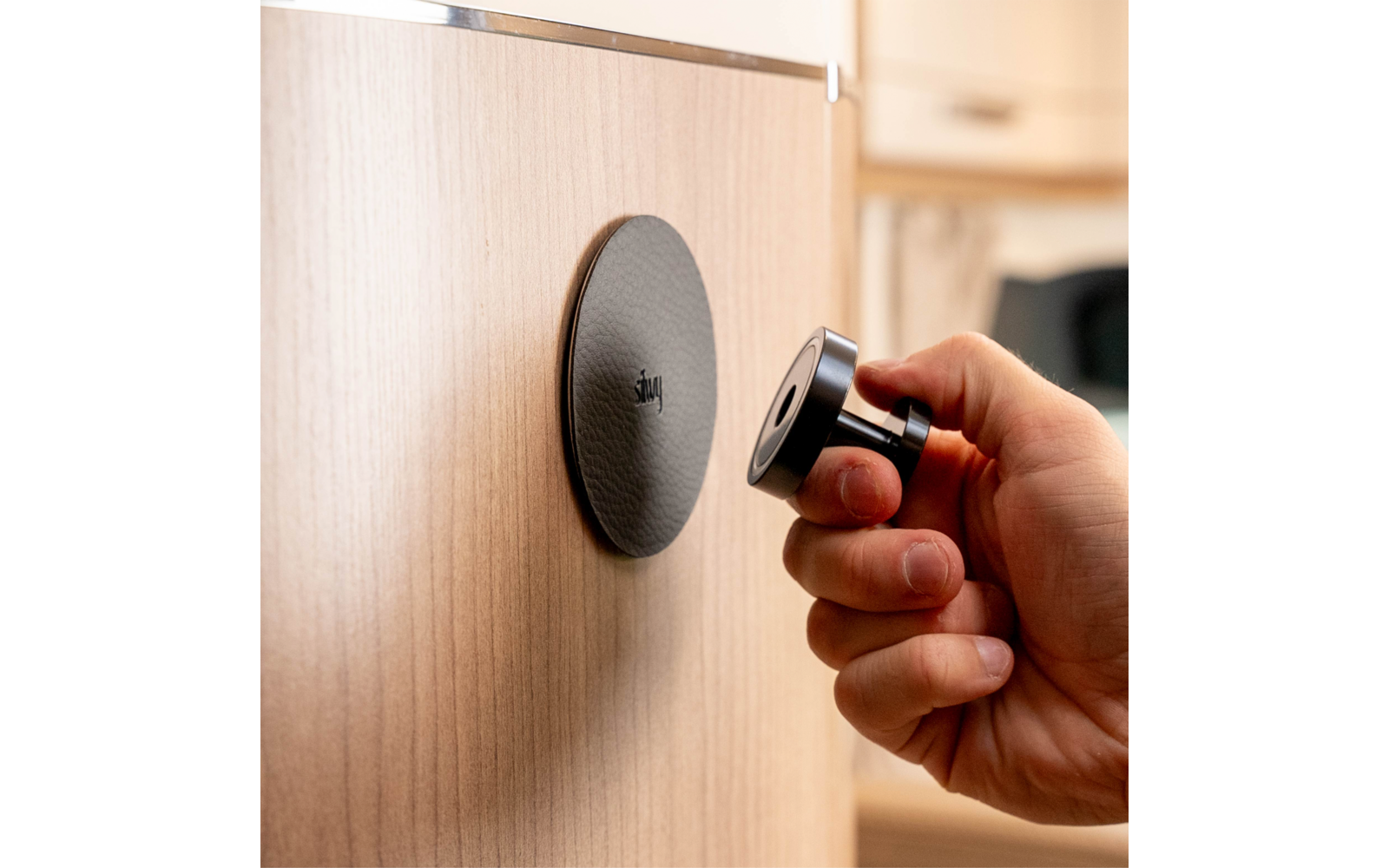 Hand houdt een zwarte magnetische meubelknop voor een licht houten oppervlak