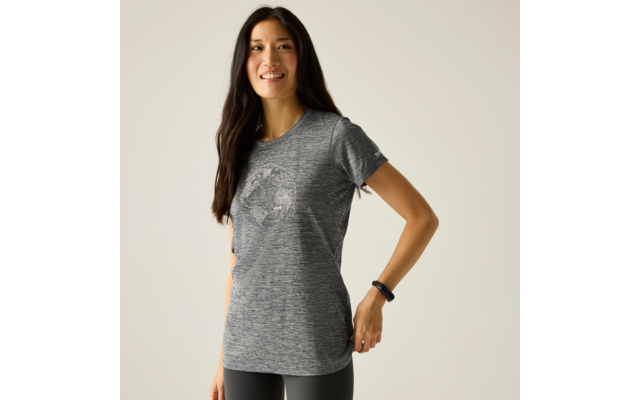 Personne aux longs cheveux foncés portant un t‑shirt gris avec motif circulaire, leggings noirs, montre fitness au poignet droit, debout devant un fond clair uni