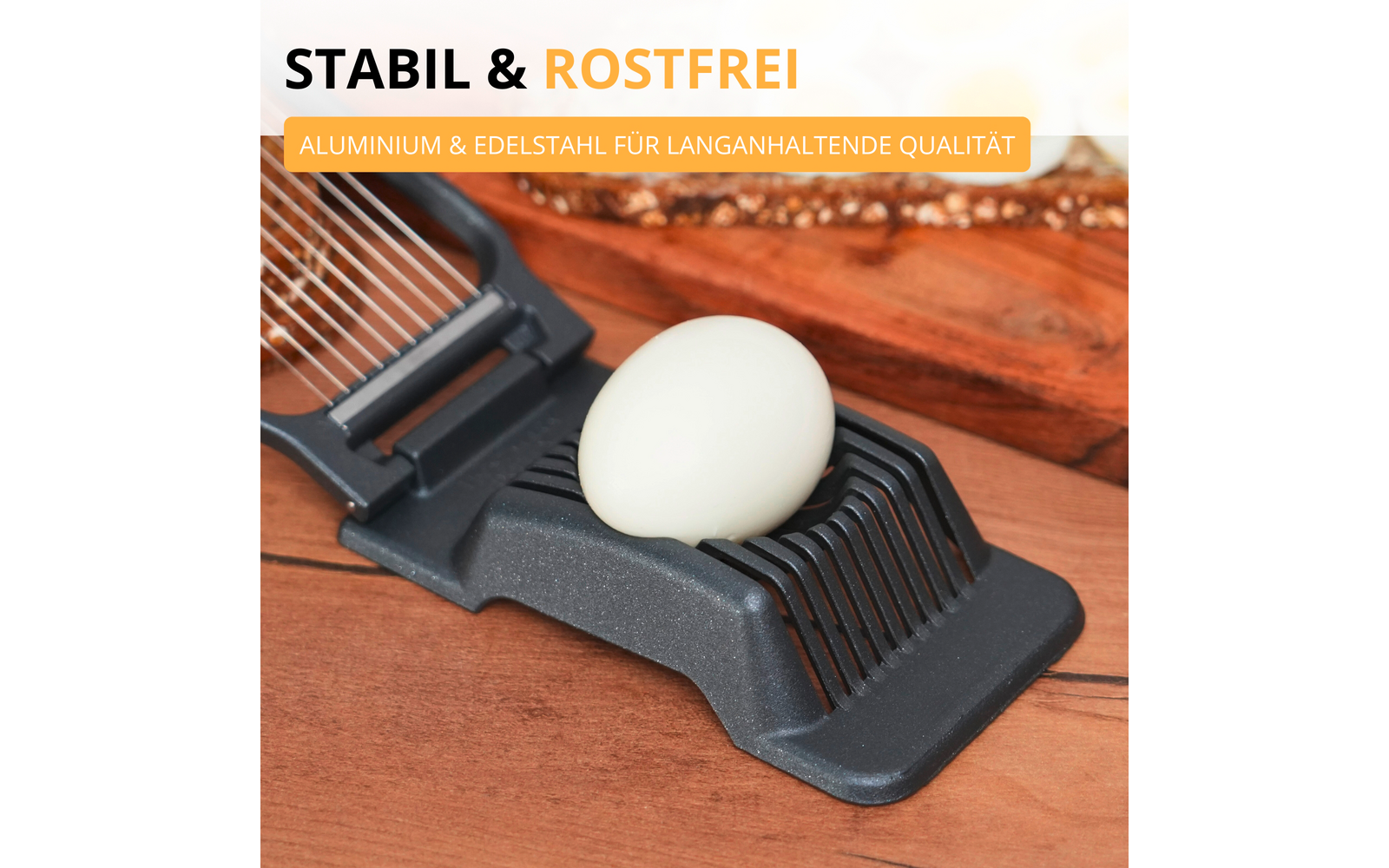 Trancheur d'œuf avec un œuf écalé sur une planche en bois; texte en arrière-plan 'STABIL & ROSTFREI' et étiquette jaune 'ALUMINIUM & EDELSTAHL FÜR LANGANHALTENDE QUALITÄT'