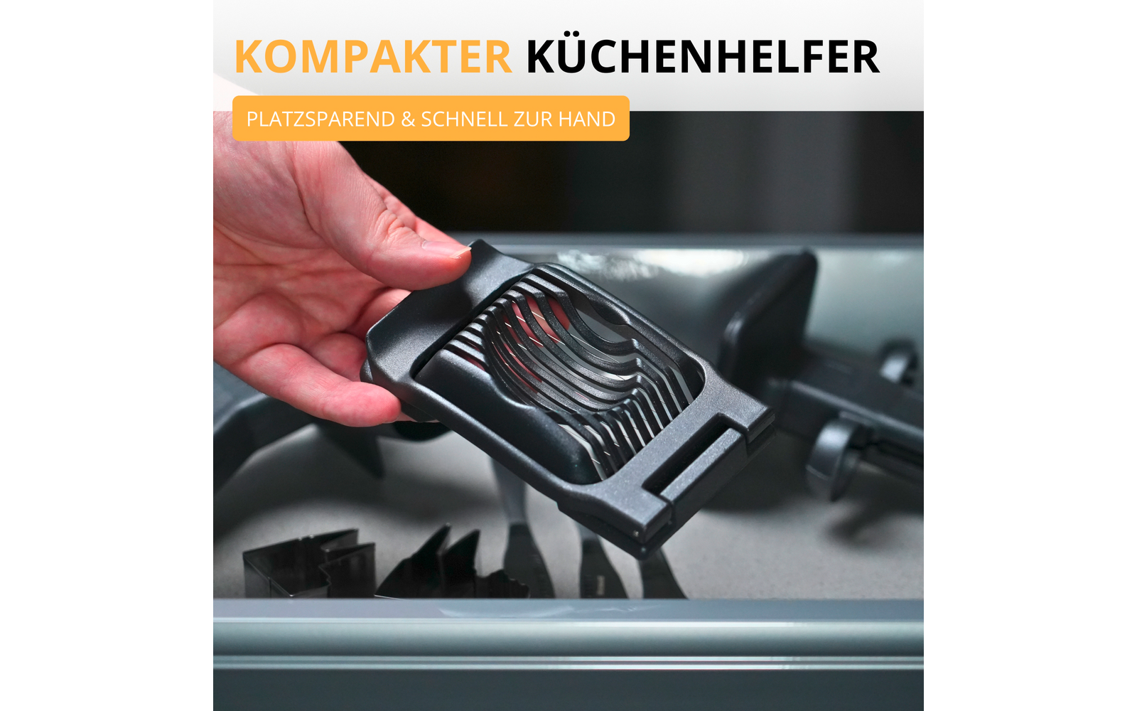 Main tenant un appareil en plastique noir avec des fentes courbes au-dessus d'un tiroir de lave-vaisselle ouvert ; en haut à gauche le texte 'KOMPAKTER KÜCHENHELFER' et une étiquette orange 'PLATZSPAREND & SCHNELL ZUR HAND'