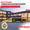 Bâtiment d'entreprise éclairé avec façade en verre et parvis pavé, petit bassin avec plantes devant; grand texte rouge 'DEUTSCHES FAMILIENUNTERNEHMEN' en haut à gauche et bandeau rouge 'SEIT 1956. KÜCHENHELFER FÜR DIE EWIGKEIT'; sceau ISO 9001:2015 en bas à gauche; logo 'WESTMARK' en bas à droite