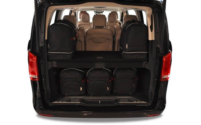 Coffre ouvert d'une camionnette noire avec cinq sacs à dos noirs (deux sur l'étagère supérieure, trois sur l'étagère inférieure), intérieur beige et plusieurs sièges avec appuie-têtes visibles