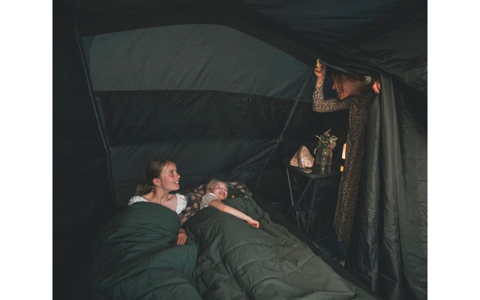 Zwei Männer liegen auf einer Wiese, ein Mann steht im Schatten eines Zeltes und schaut zu ihnen