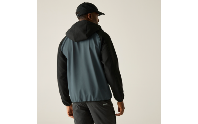 Person von hinten, trägt schwarze Schirmmütze, Kapuzenjacke mit blaugrauem Rücken und schwarzen Ärmeln, schwarze Hose mit kleinem Logo, heller einfarbiger Hintergrund