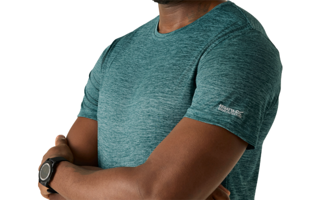 Mann mit verschränkten Armen, trägt ein türkisfarbenes kurzärmeliges T-Shirt und eine Smartwatch, schaut in die Kamera vor hellem einfarbigem Hintergrund