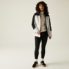 Vrouw met krullend haar draagt een wit-zwart sportjack, zwarte joggingbroek en sportschoenen, staat voor een lichte achtergrond