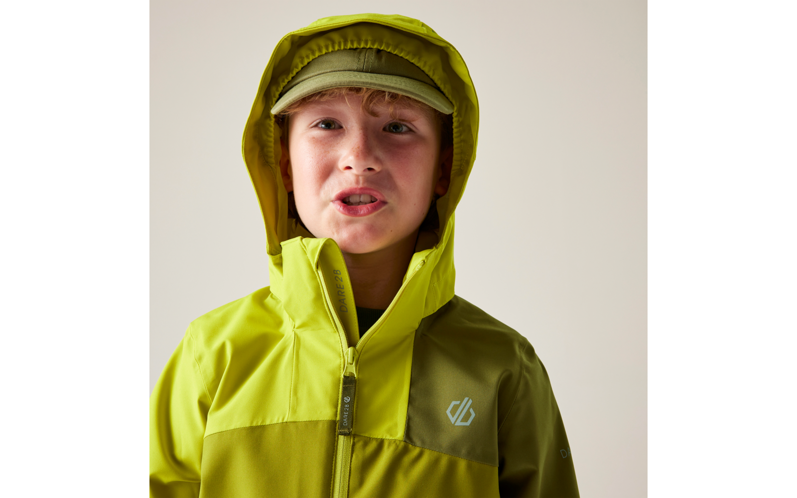 Kind mit grüner Kapuzenjacke und passender Kappe vor hellem Hintergrund