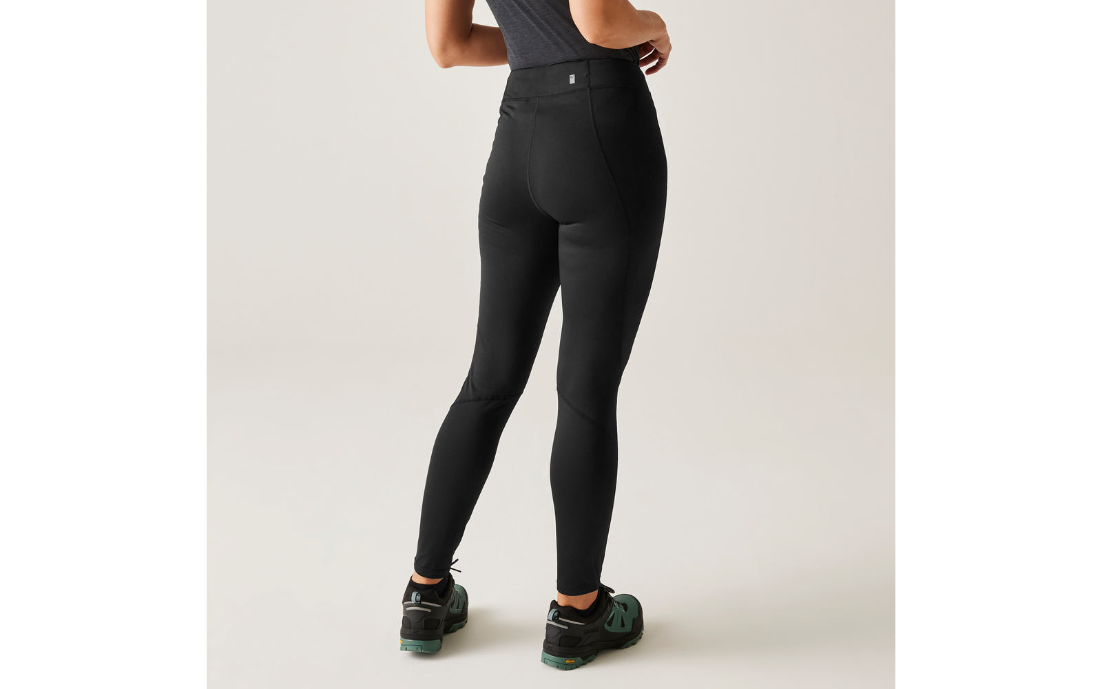 Frau von hinten mit schwarzen Leggings und Sportschuhen vor hellem Hintergrund