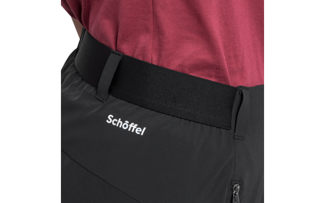 Nahaufnahme der Taille mit schwarzer Hose mit 'Schöffel'-Logo, elastischem Bund und Reißverschlusstasche, bordeauxfarbenes T-Shirt im Bund