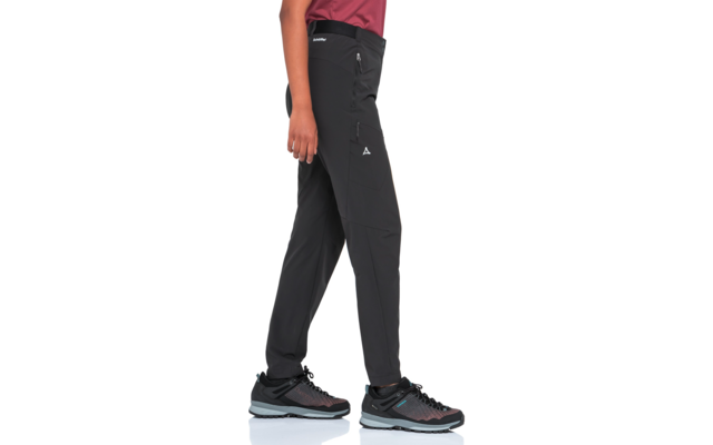 Unterkörper einer Person von der Hüfte abwärts, Saum eines roten Oberteils sichtbar, schwarze Outdoorhose mit seitlicher Reißverschlusstasche und kleinem Logo, dunkle Sportschuhe