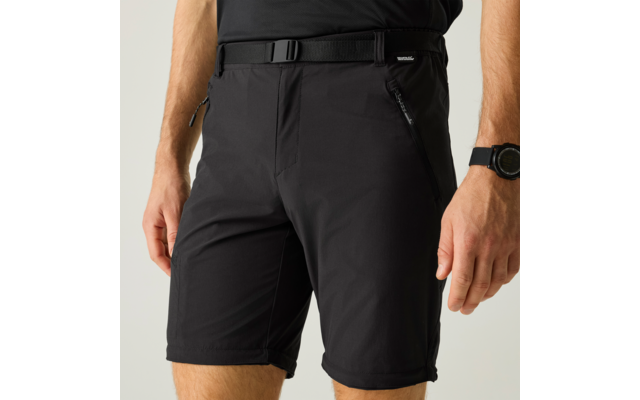 Unterkörper einer Person in schwarzem T-Shirt und schwarzen Shorts mit Gürtel und Reißverschlusstaschen, sichtbare Oberschenkel, Handgelenk mit schwarzer Uhr