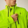 Oberkörper einer Person in neon-gelb-grüner Jacke mit schwarzen Reißverschlüssen und Brustlogo; Hand hält den Reißverschluss