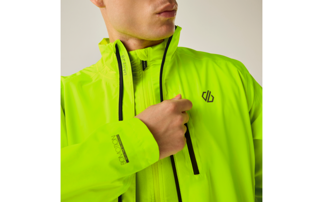 Oberkörper einer Person in neon-gelb-grüner Jacke mit schwarzen Reißverschlüssen und Brustlogo; Hand hält den Reißverschluss