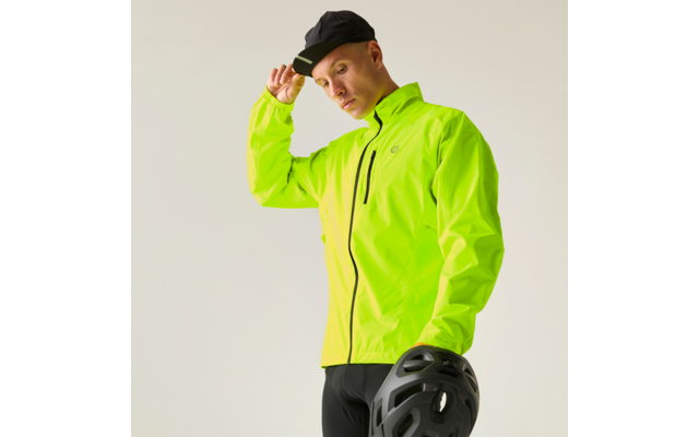 Person mit neongrüner Jacke und schwarzer Kappe, hält einen schwarzen Fahrradhelm vor hellem Hintergrund