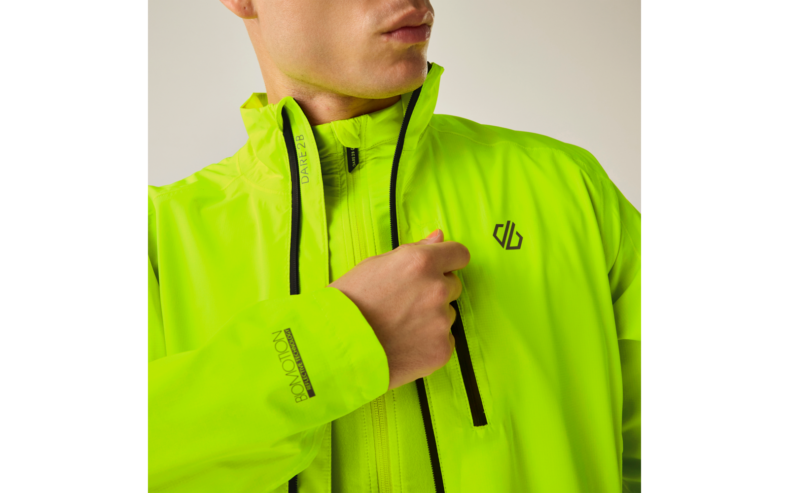 Oberkörper einer Person in neon-gelb-grüner Jacke mit schwarzen Reißverschlüssen und Brustlogo; Hand hält den Reißverschluss