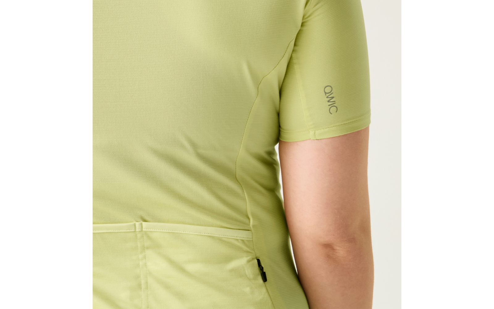 Rückenansicht einer Person in hellem limonengrünem, kurzärmligem Shirt mit Beschriftung QWIC auf der Ärmel, Rückentasche, kleinem schwarzem Seitenschild und sichtbarem Unterarm
