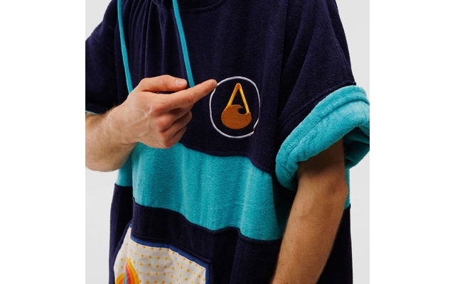 Eine Person hebt den Ärmel eines blau-türkis gestreiften Pullovers hoch, auf der Brust ist ein orange-weißes Dreieck zu sehen