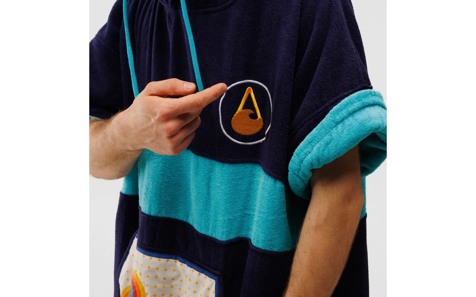 Eine Person hebt den Ärmel eines blau-türkis gestreiften Pullovers hoch, auf der Brust ist ein orange-weißes Dreieck zu sehen