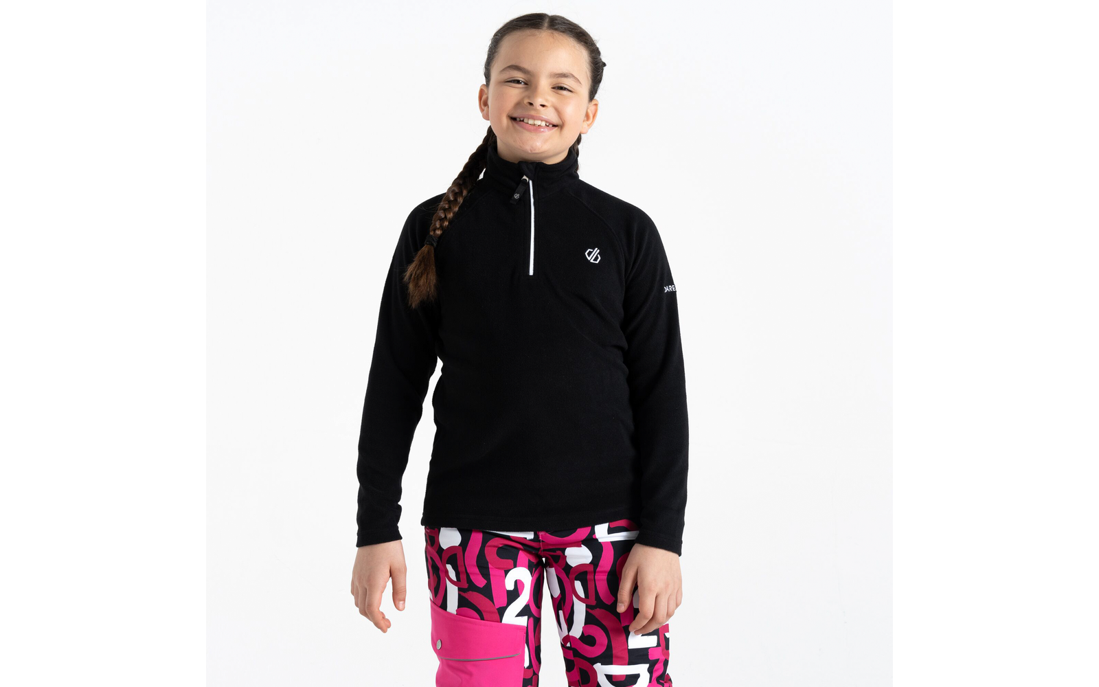 Mädchen trägt schwarzen Pullover und bunte Hose vor weißem Hintergrund