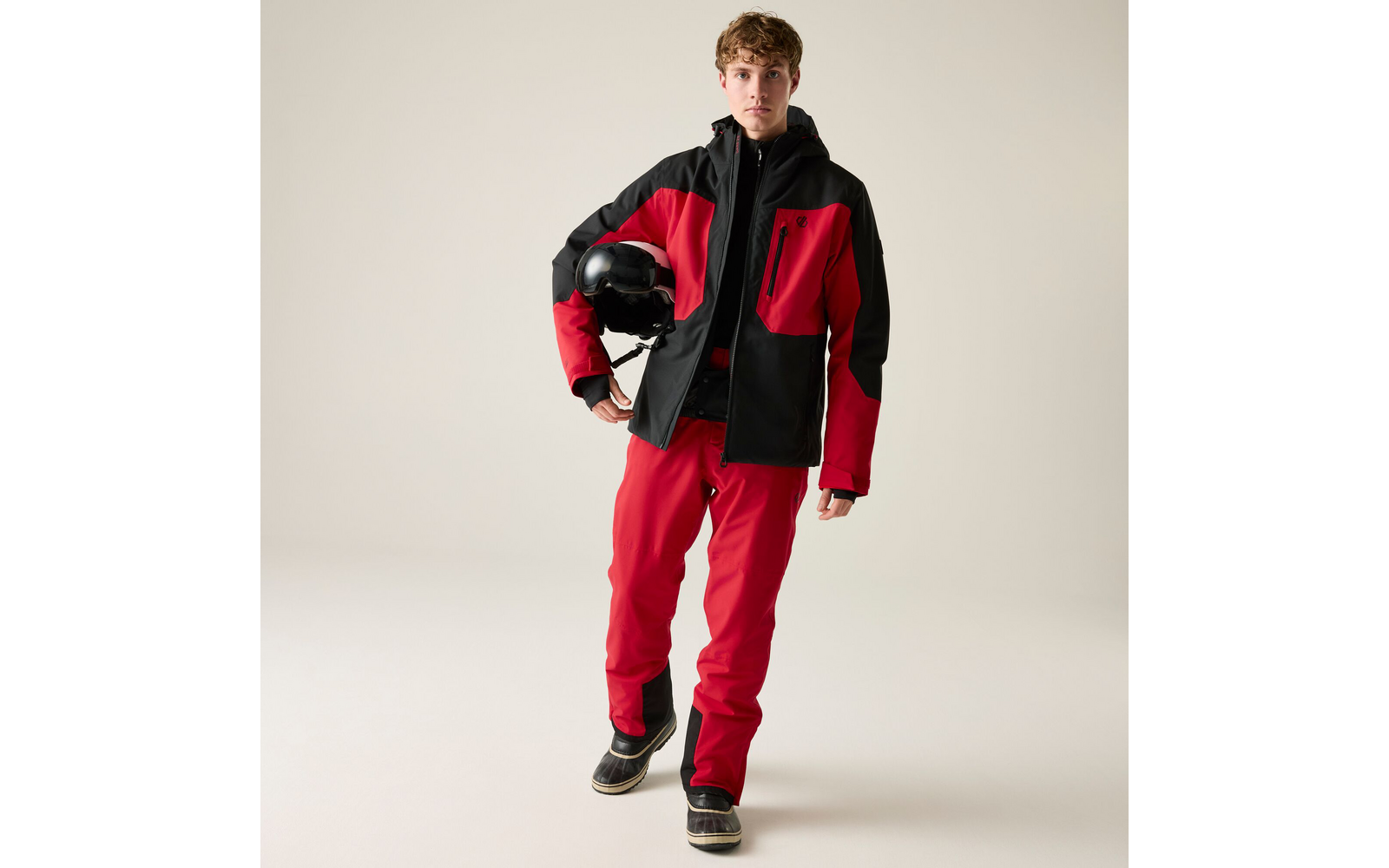 Person in roter und schwarzer Jacke und roter Hose, steht und hält einen schwarzen Helm
