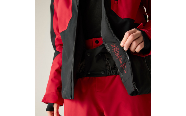 Nahaufnahme einer Person in roter und schwarzer Jacke und roter Hose; Jacke geöffnet, innere Reißverschlussklappe mit kleinen Symbolen, Hände halten die Klappe, heller Hintergrund