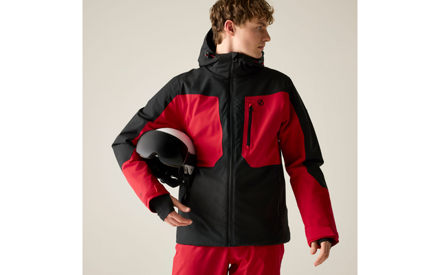 Person in roter und schwarzer Jacke und roten Hosen hält einen schwarz-weißen Helm, Blick nach rechts
